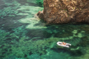 Sicily - Sunny impressions of the Aeolian Islands, also known as Aeolian Islands or Isole Eolie: Lipari, Stromboli, Salina, Vulcano, Panarea, Filicudi and Alicudi. Crystal clear water at Cala Junco, Panarea. Couple in an inflatable boat. Sicily - Sunny impressions of the Aeolian Islands, also known as Aeolian Islands or Isole Eolie: Lipari, Stromboli, Salina, Vulcano, Panarea, Filicudi and Alicudi. Crystal clear water at Cala Junco, Panarea. Couple in an inflatable boat.